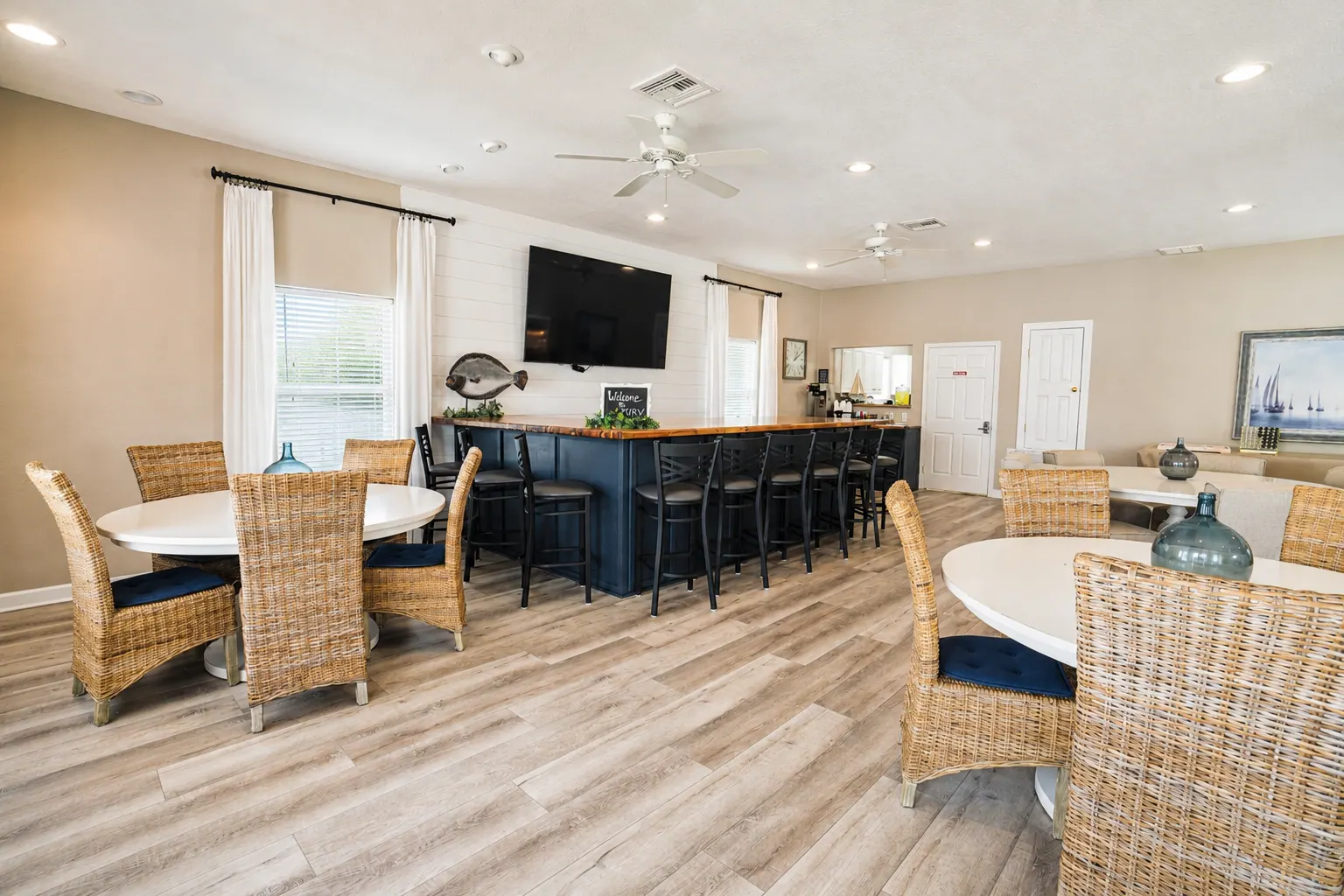 Resort clubhouse interior with a navy bar, wicker seating, round tables, and coastal decor