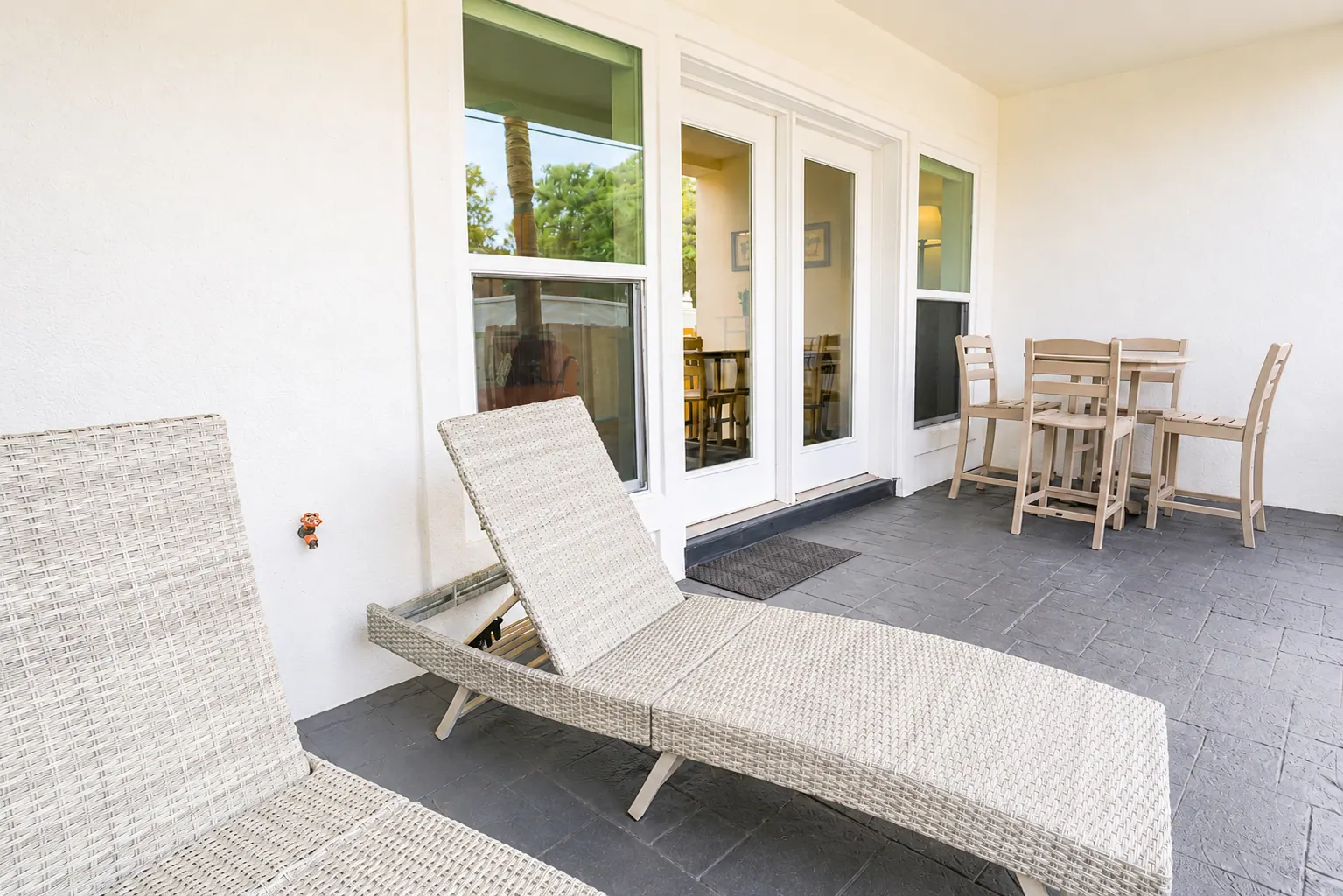 Ground-floor condo patio with wicker chaise loungers beside sliding glass doors