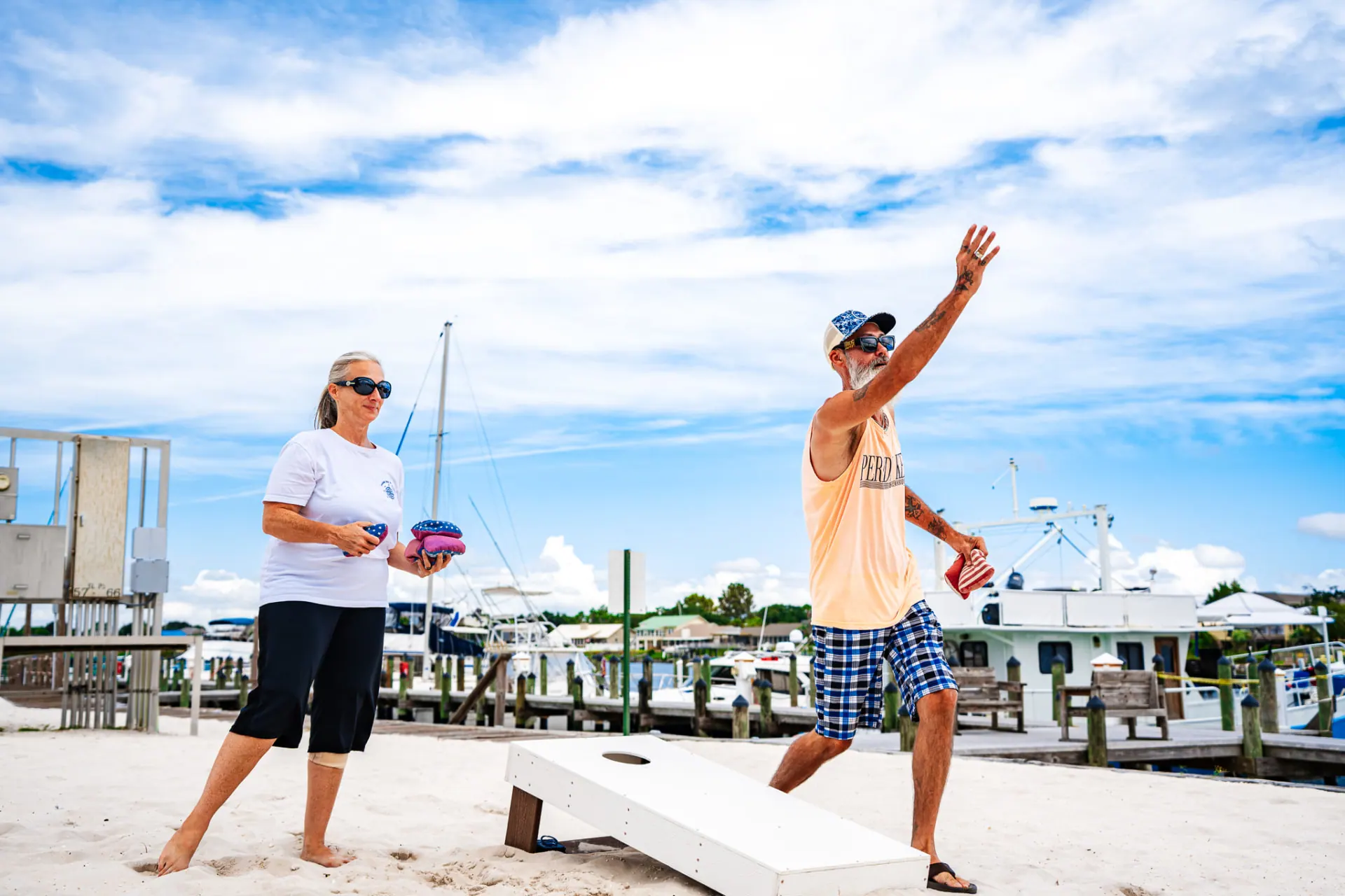 Cornhole game on the beach with boats in the marina behind