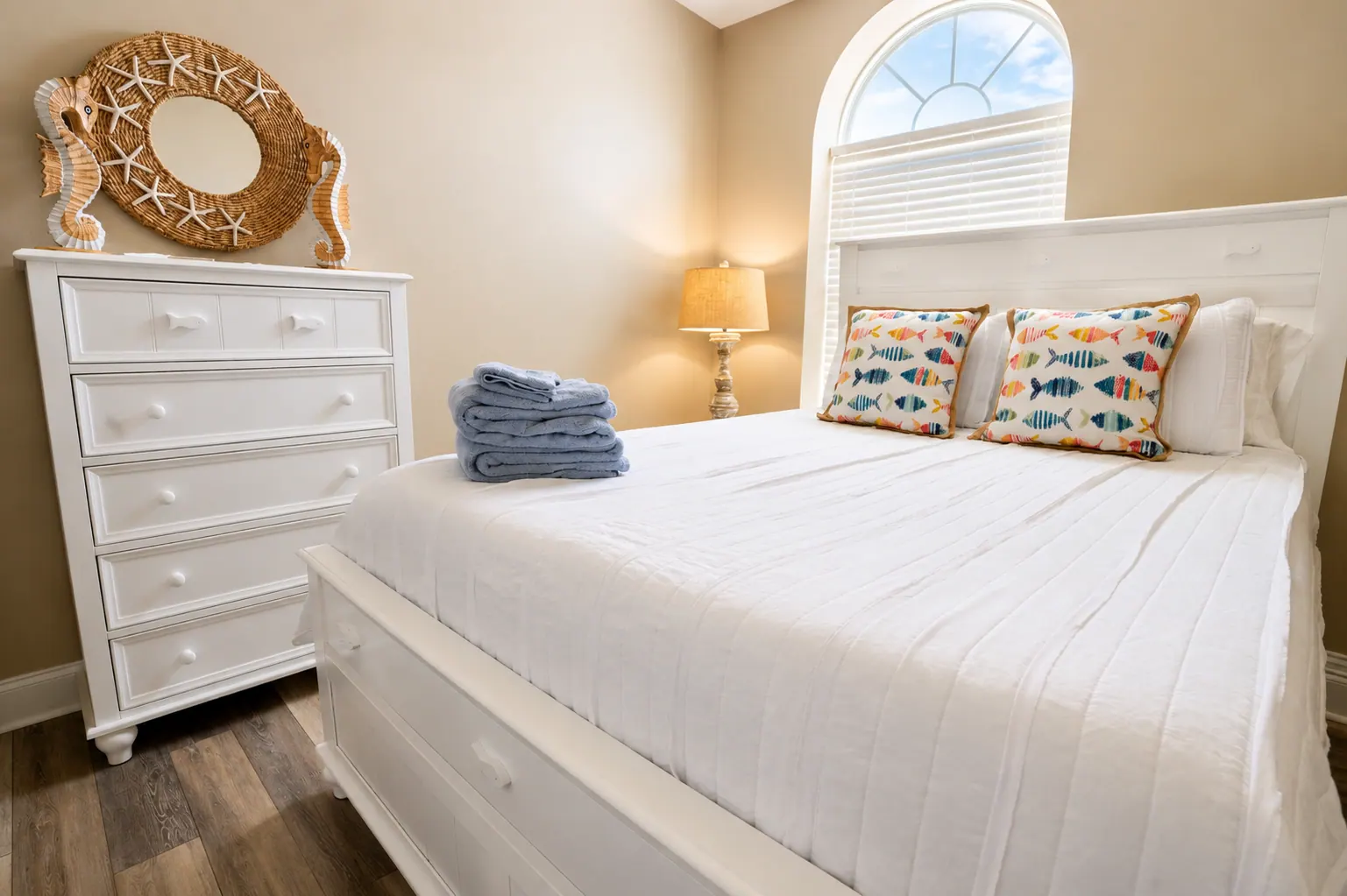 Condo bedroom with white bed, fish-print pillows, and seashell mirror