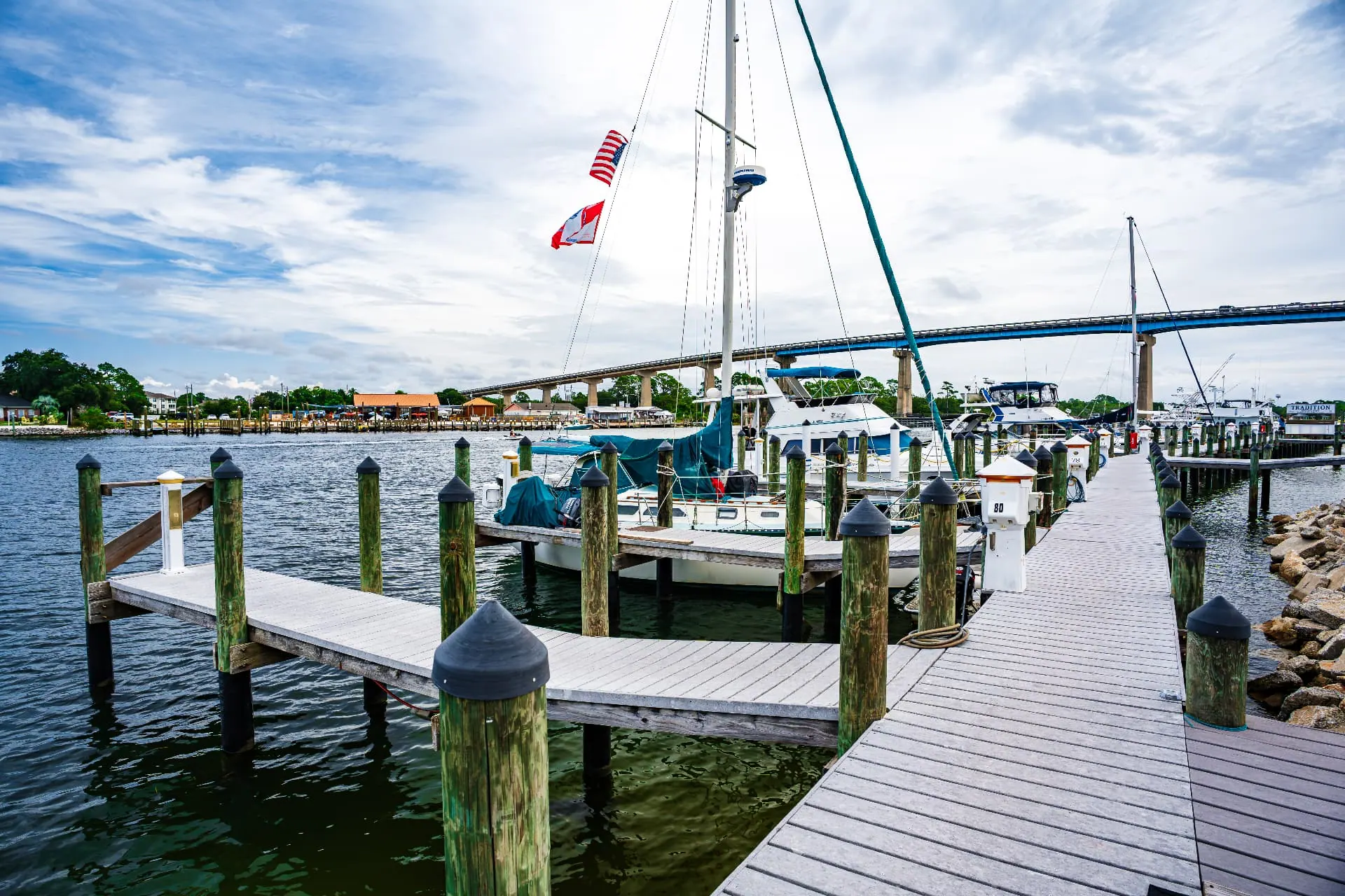 Wooden marina pier with a furled sailboat and motorboats docked beneath the Perdido Key bridge