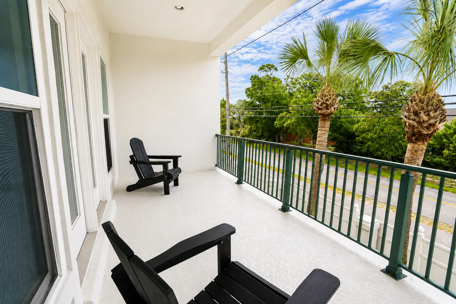 Sunny condo balcony with two black Adirondack chairs overlooking palms and a quiet street