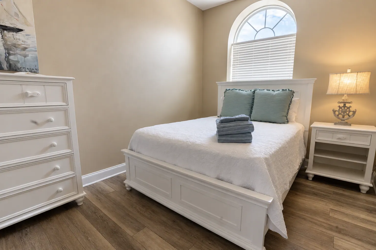 Condo bedroom with white coastal furniture, arched window, and sage pillows