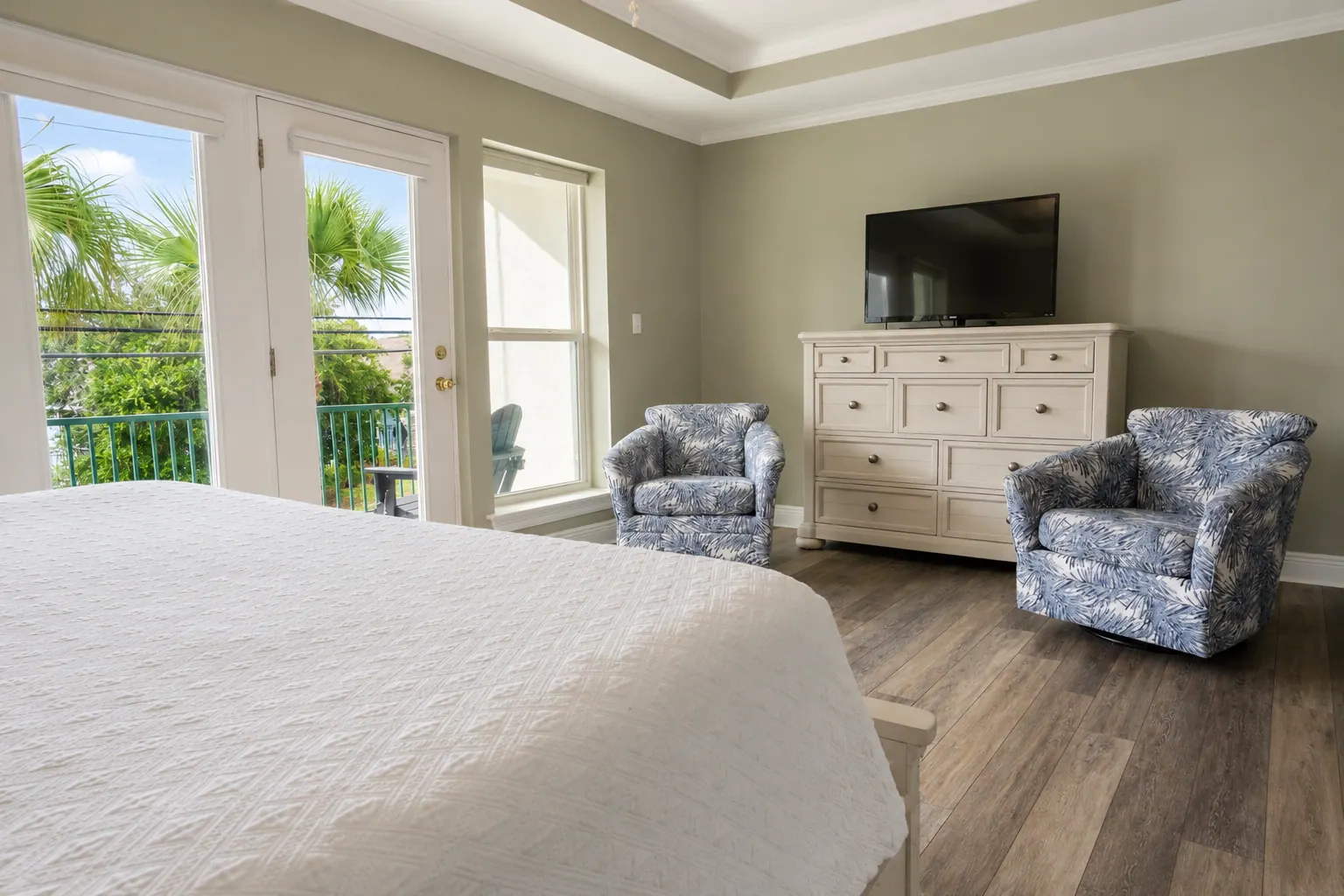 Condo guest bedroom with swivel chairs, dresser, TV, and balcony doors