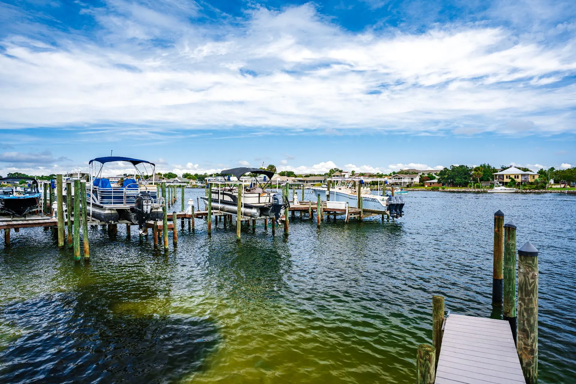 Powerboats and pontoons resting on mechanical lifts along the wooden marina docks