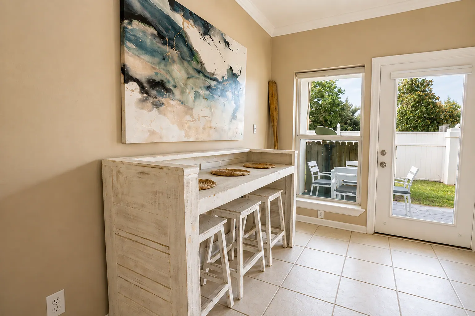 Whitewashed high-top bar table with stools and a coastal oar in a condo dining nook